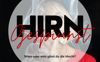 Eine Person in einem roten Hemd hält ein Mikrofon hinter einem rauchigen Hintergrund mit den Texten „HIRN Gespinst“ und „Wem oder was gibst du die Macht?“ auf Deutsch.