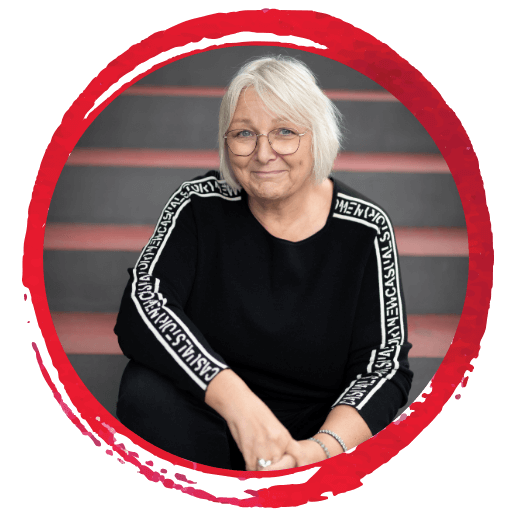 Person mit kurzen weißen Haaren und Brille, sitzt auf einer Treppe und trägt einen schwarzen Pullover mit Textmuster auf den Ärmeln. Roter kreisförmiger Rand um das Bild. Person mit kurzen weißen Haaren und Brille, sitzt auf einer Treppe und trägt einen schwarzen Pullover mit Textmuster auf den Ärmeln. Roter kreisförmiger Rand um das Bild.